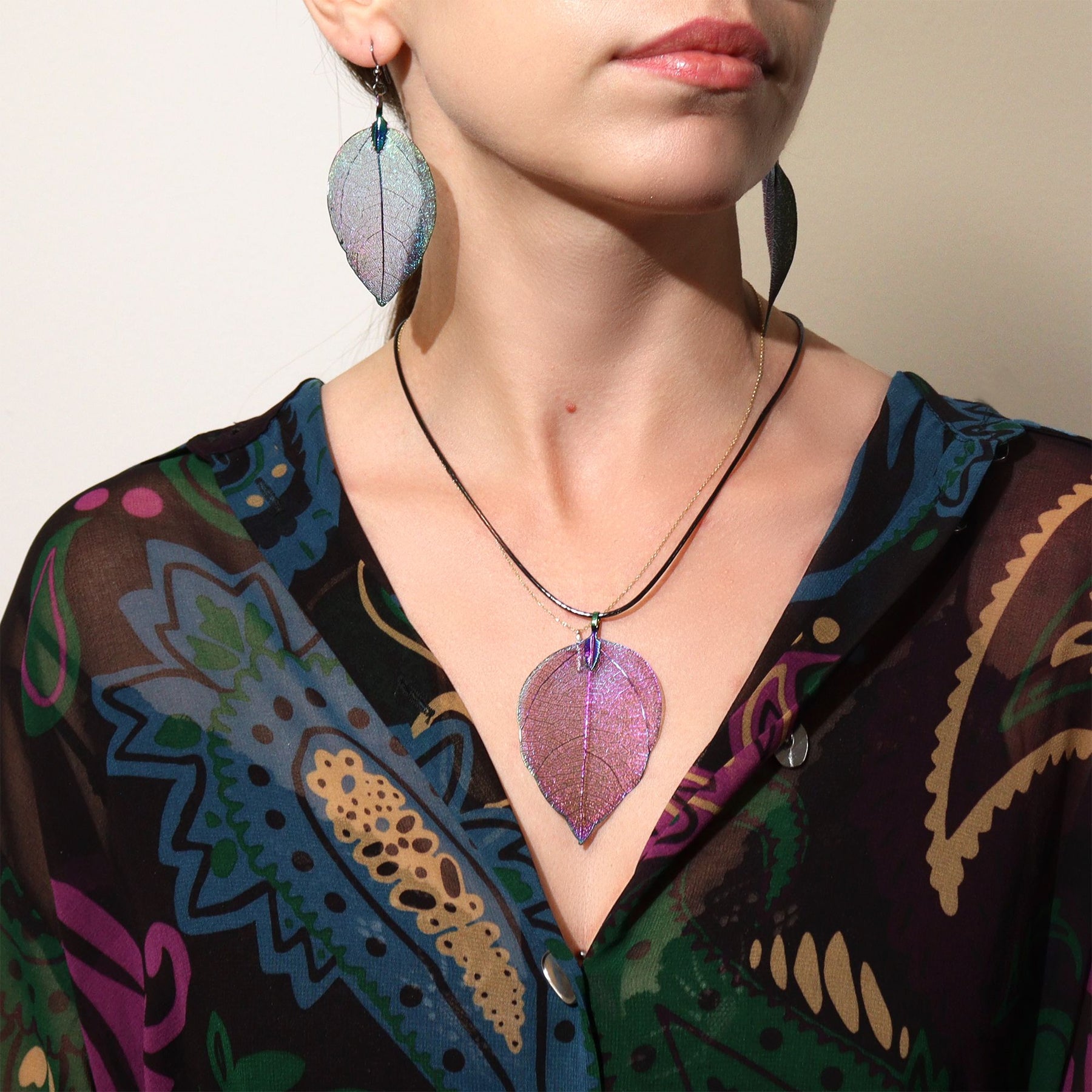 Person wearing a colorful patterned garment with a leaf-shaped necklace and earrings.