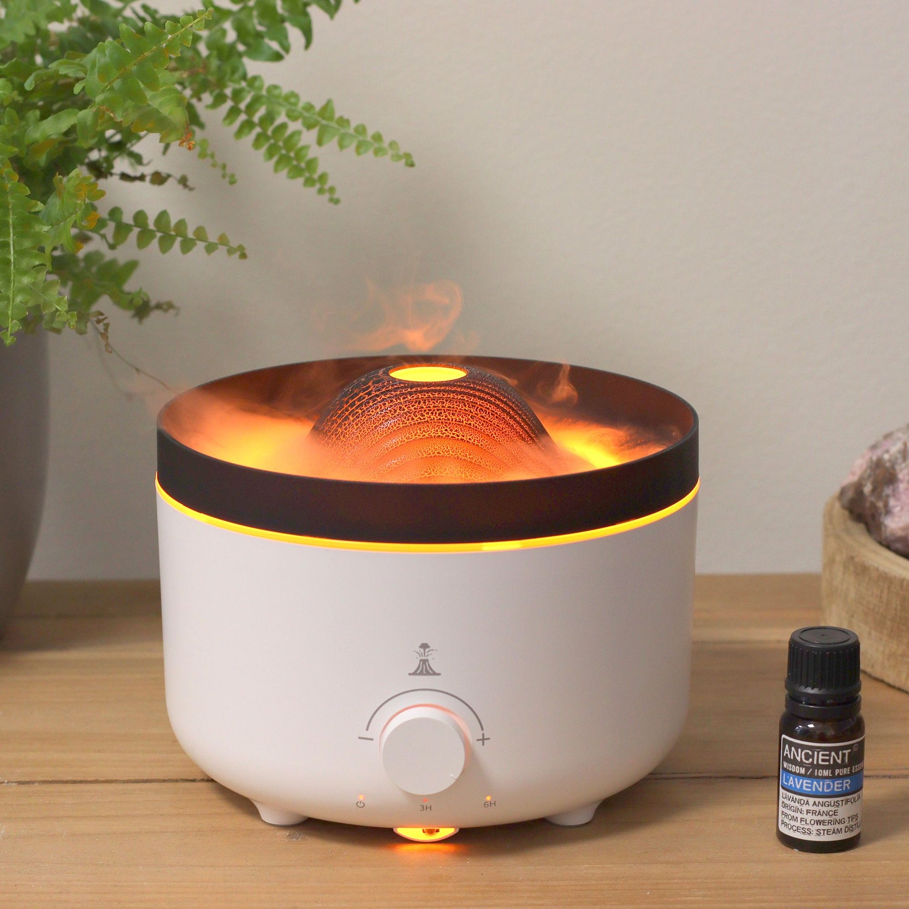 Large black volcano aroma diffuser erupting with swirling coloured mist and glowing LED ring, essential oil bottle beside