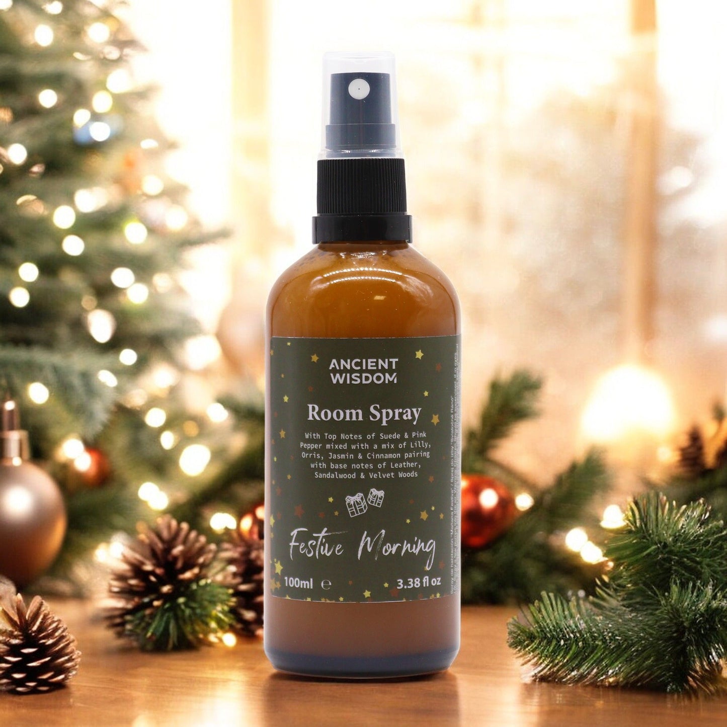 100ml Festive Morning room spray in matte amber bottle with gold sprayer, surrounded by cinnamon sticks, jasmine flowers and velvet ribbon on dark wooden table