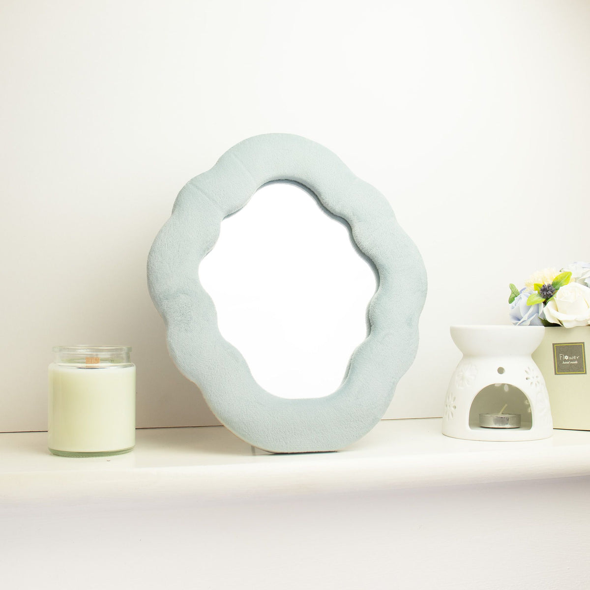 Soft squiggly cloud mirror in serene Cloud Blue velvet frame with smooth rounded silhouette, freestanding on white dressing table with soft natural light reflecting in glass
