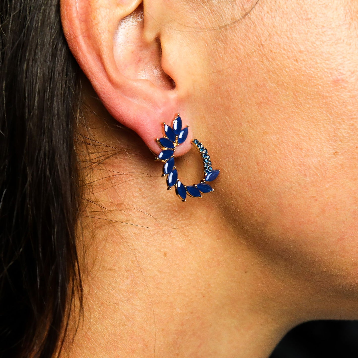 Close-up of an ear wearing a blue gemstone hoop earring.