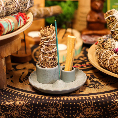 Matte blue ceramic lotus flower smudge holder with Palo Santo stick burning, white sage bundle and incense cone, styled on altar with crystals and candles