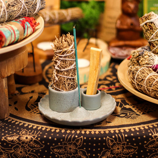Matte blue ceramic lotus flower smudge holder with Palo Santo stick burning, white sage bundle and incense cone, styled on altar with crystals and candles