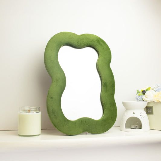 Soft squiggly large cloud mirror in earthy moss green velvet frame with organic curved silhouette, freestanding on white console table with soft natural light reflecting in glass