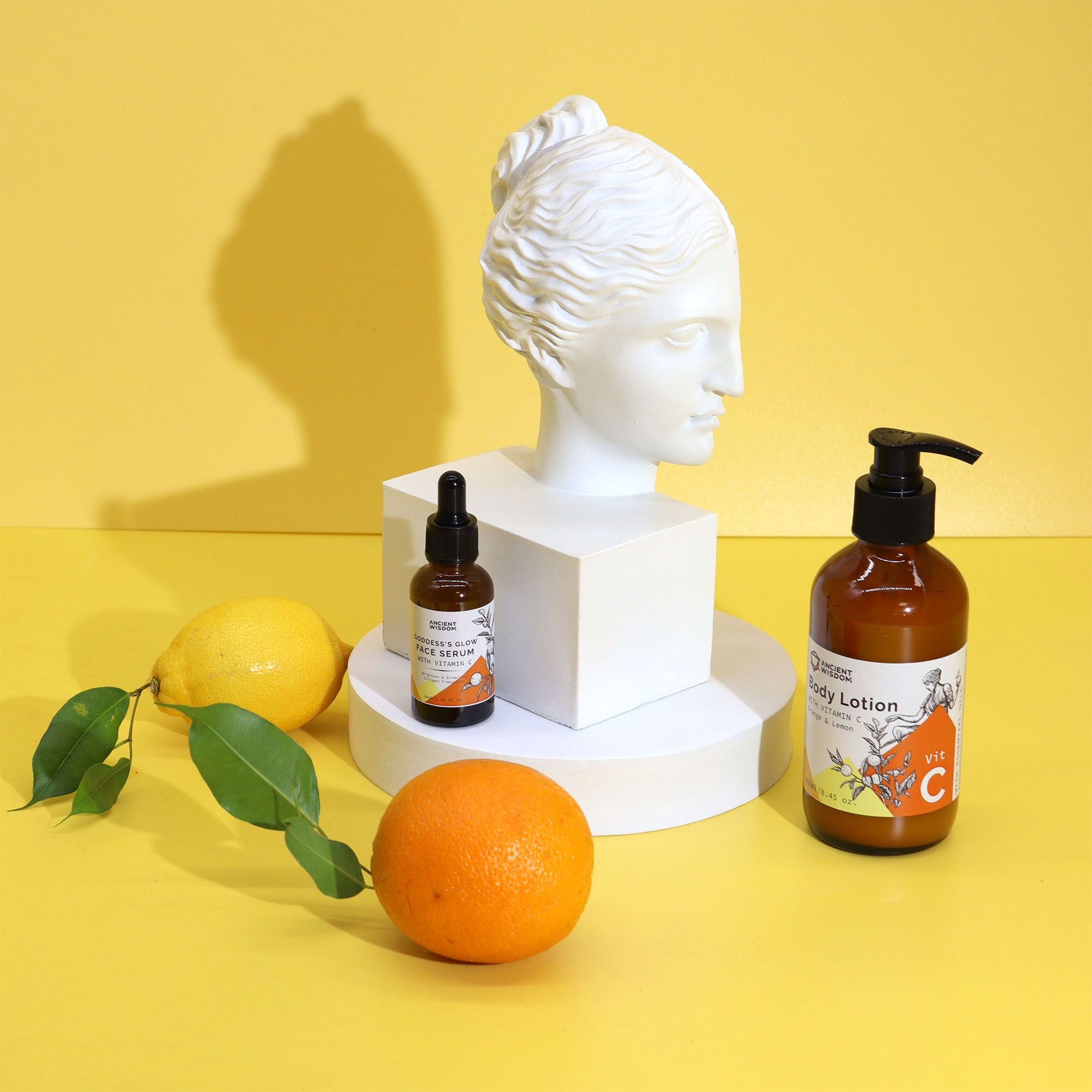 Elegant amber glass dropper bottle of Goddess’s Glow Vitamin C face serum with fresh orange slices, cranberries, grapefruit and aloe leaves on marble with soft golden light