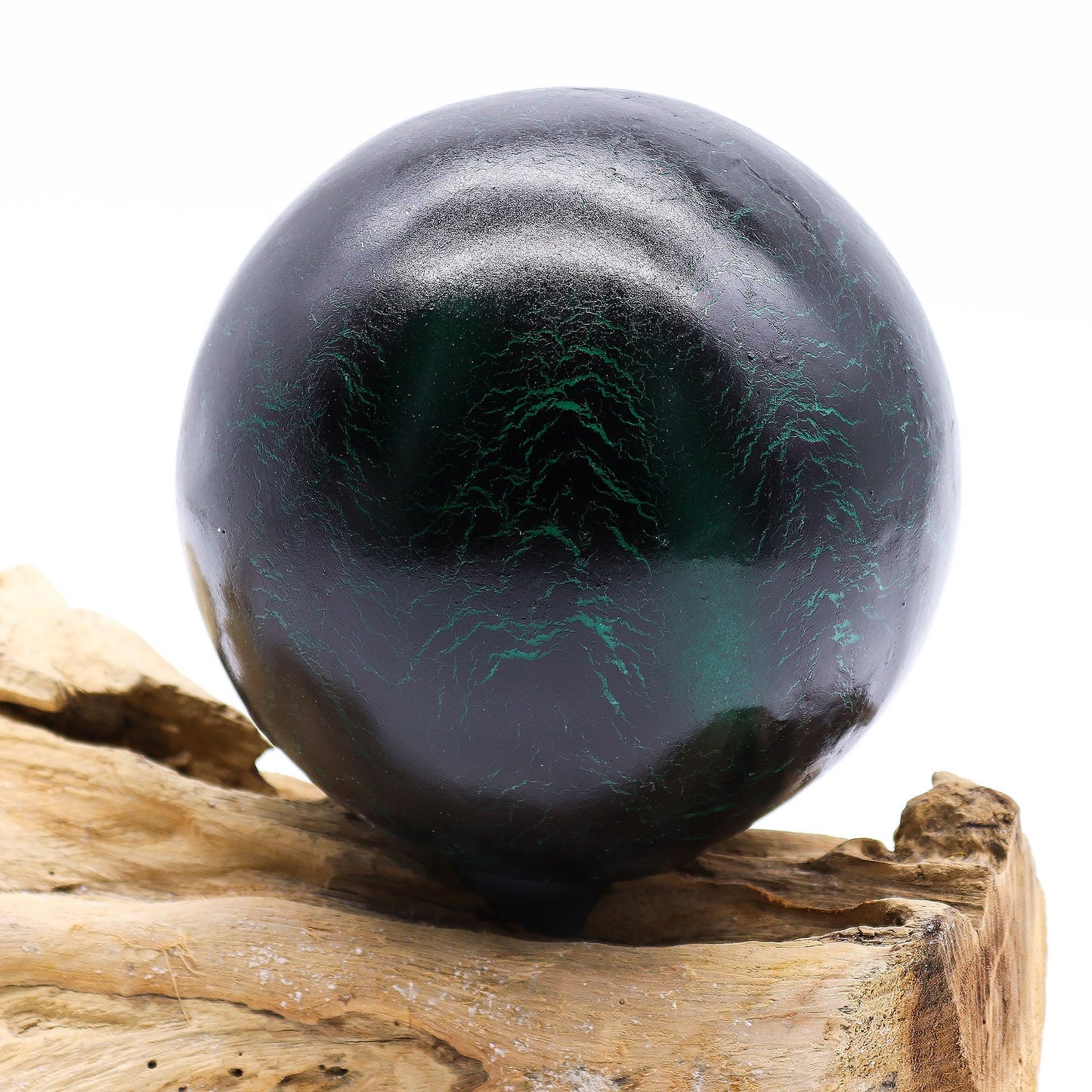 Emerald crackle glass sphere glowing atop unique twisted driftwood base on dark wooden side table with books and plants at night