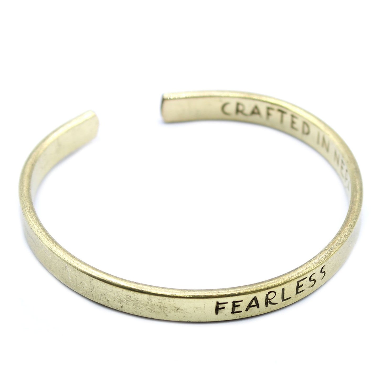 Golden brass mantra cuff engraved “FEARLESS” on wrist, Himalayan prayer flags and snow-capped peaks in soft background light