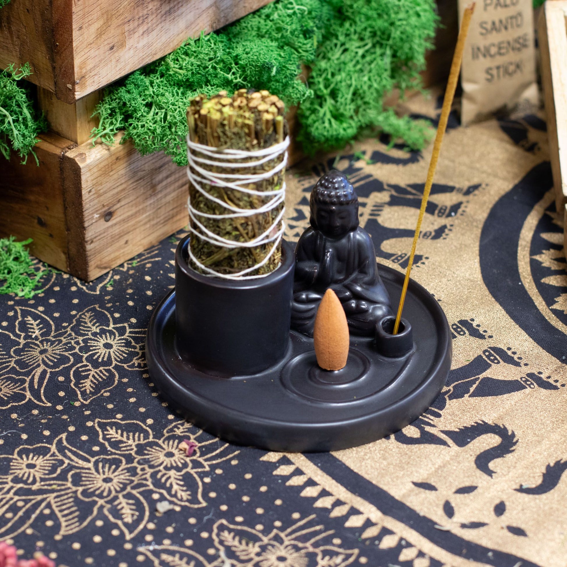 Incense burner with a Buddha statue and incense sticks on a decorative mat.