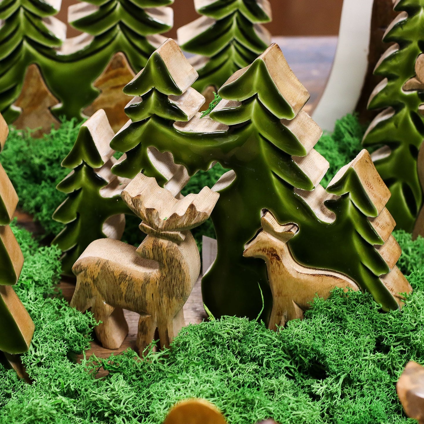 3D mango wood deer in forest decoration with two standing deer, green enamel trees and layered woodland scene on mantel with fairy lights and pine cones