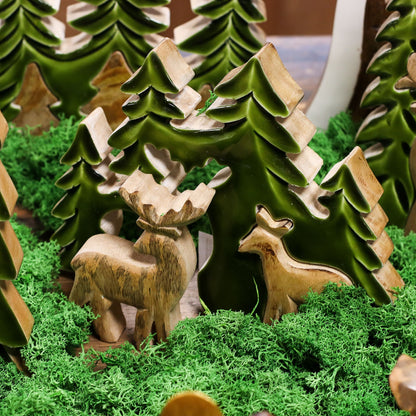 3D mango wood deer in forest decoration with two standing deer, green enamel trees and layered woodland scene on mantel with fairy lights and pine cones