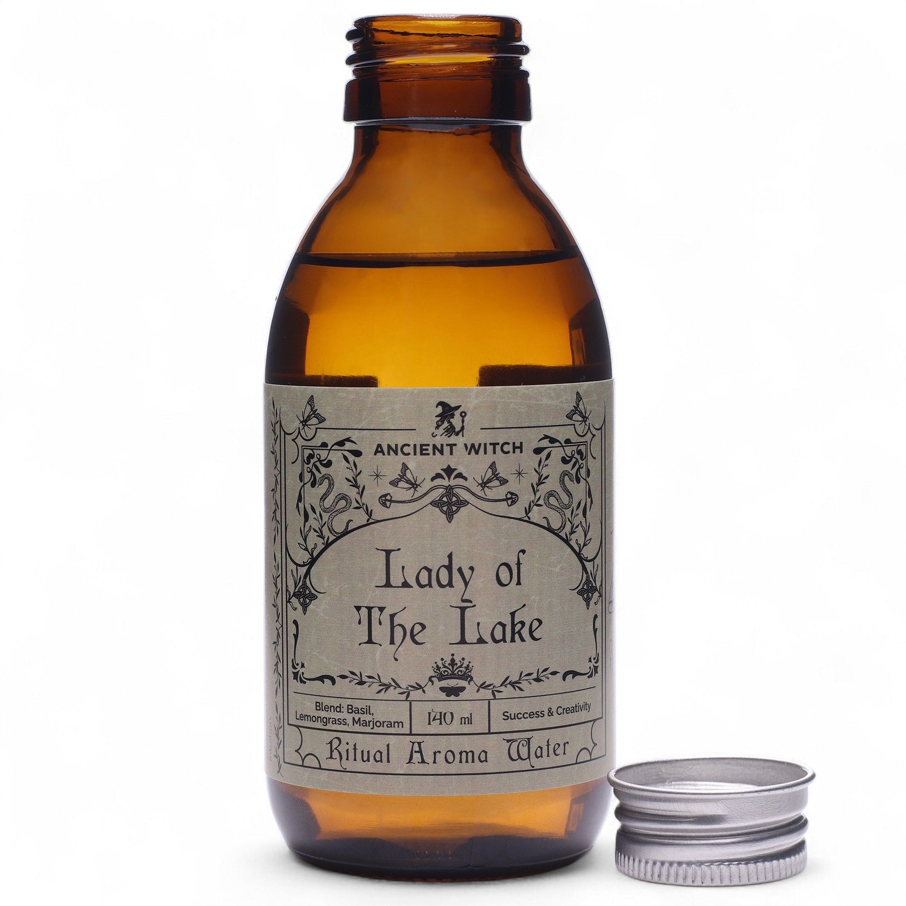 140ml amber glass bottle of Lady of the Lake ritual water with sword-in-lake label, surrounded by fresh basil, lemongrass, misty water and Excalibur sword