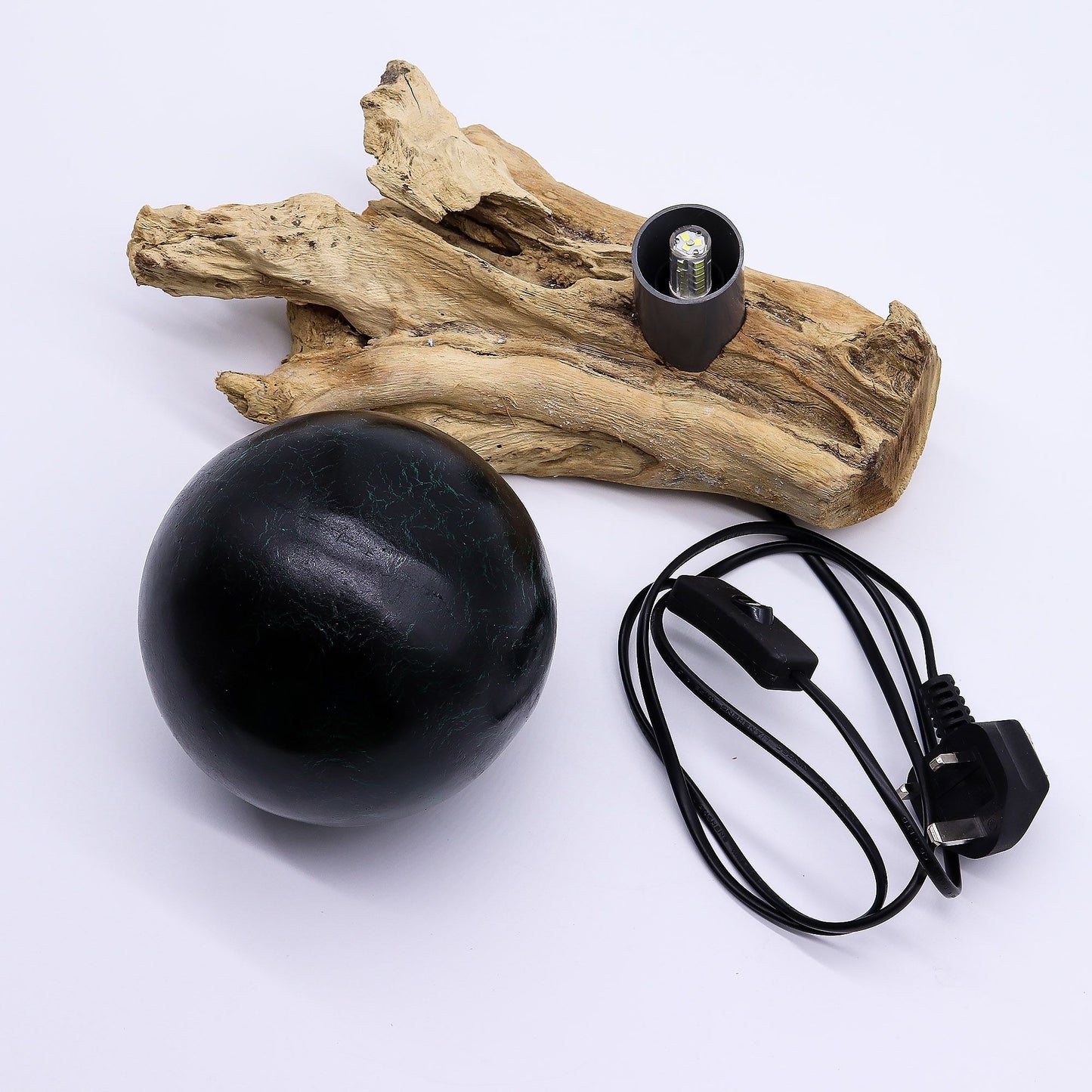Emerald crackle glass sphere glowing atop unique twisted driftwood base on dark wooden side table with books and plants at night