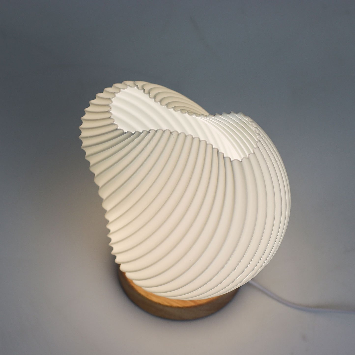 Close-up of lamp’s textured honeycomb pattern and soft diffused light, showing elegant twisted shell-like silhouette and wooden base detail