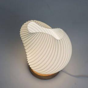 Close-up of lamp’s textured honeycomb pattern and soft diffused light, showing elegant twisted shell-like silhouette and wooden base detail