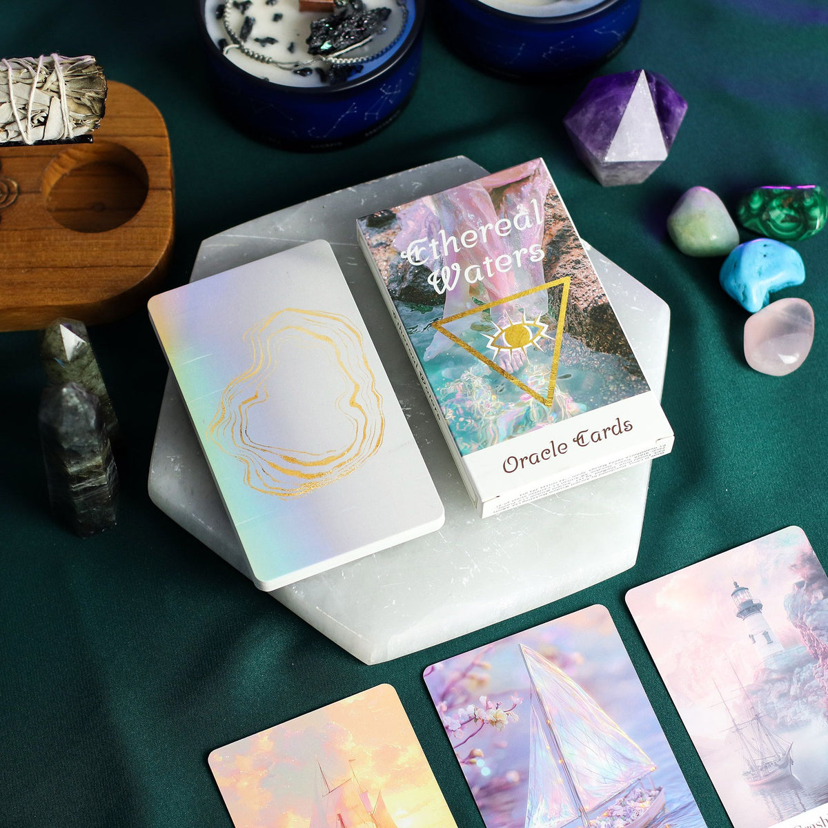 Oracle cards with 'Ethereal Waters' set surrounded by crystals and a wooden tool on a green surface.