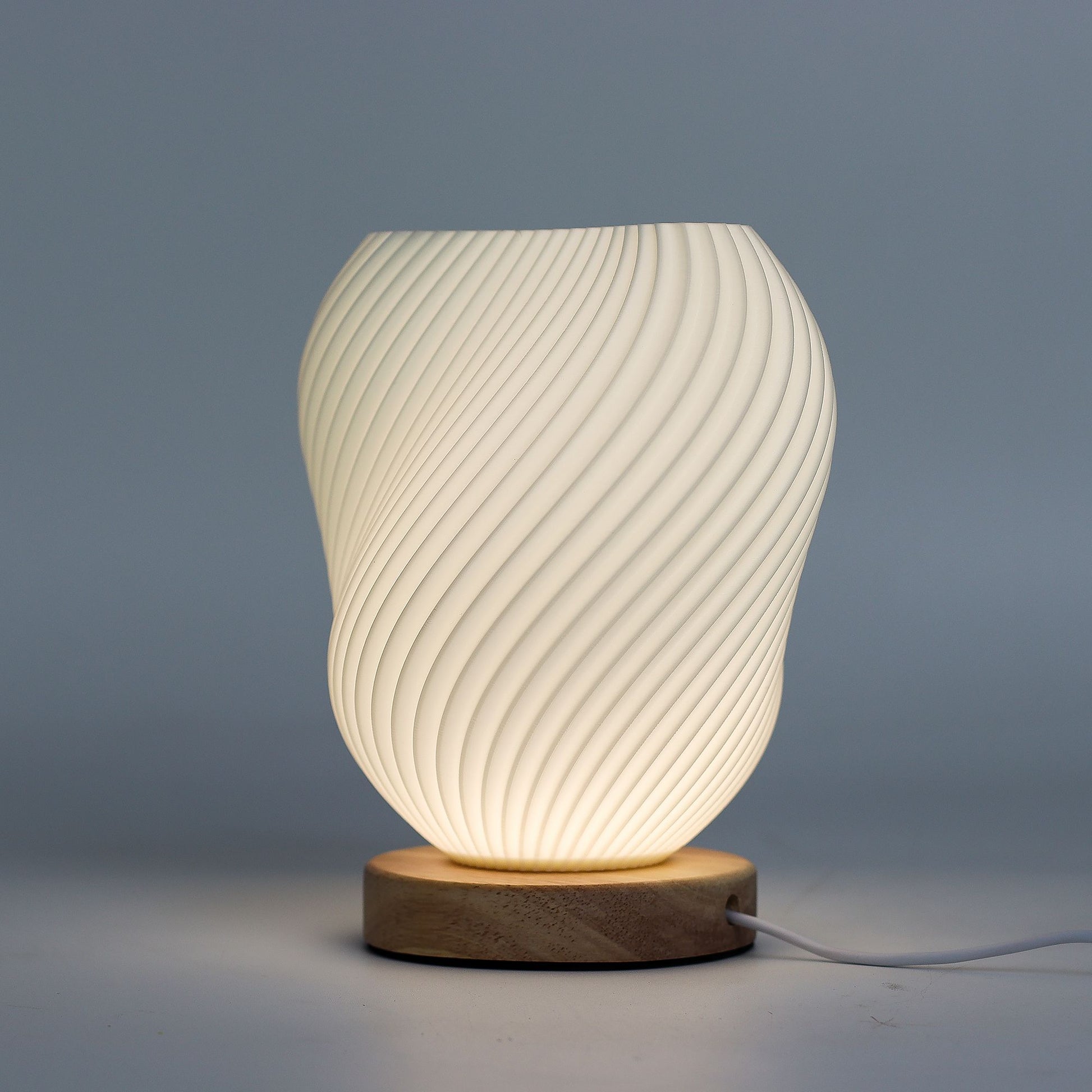Close-up of lamp’s textured honeycomb pattern and soft diffused light, showing elegant twisted shell-like silhouette and wooden base detail