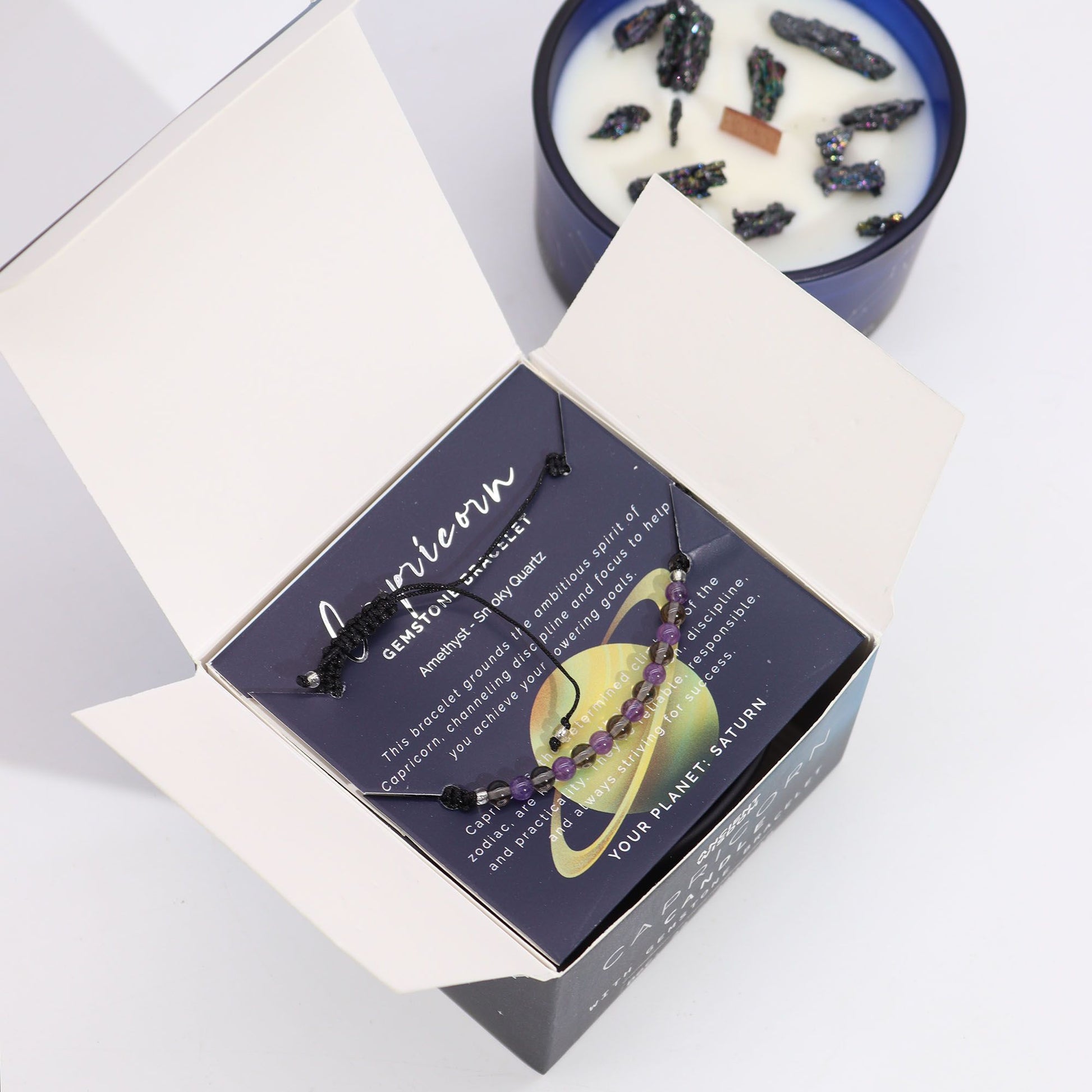 Navy & gold Capricorn zodiac candle burning beside matching amethyst & smoky quartz bracelet, styled with Capricorn constellation card and mountain crystals