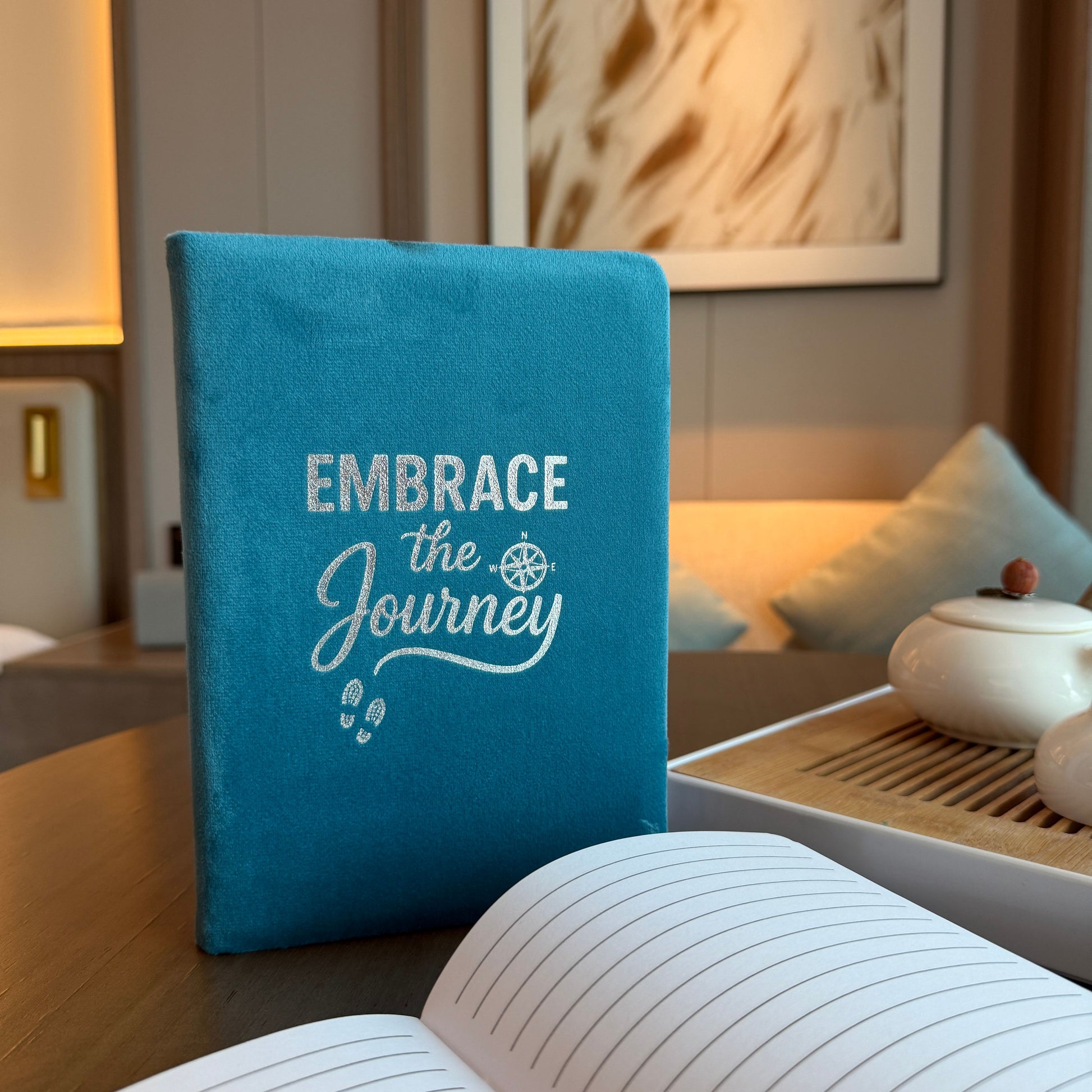 Blue notebook with 'Embrace the Journey' text on a wooden table in a room setting.