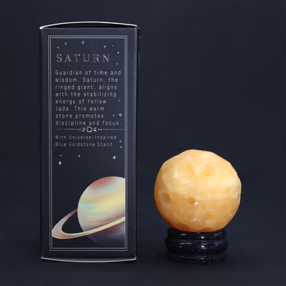 40mm yellow jade Saturn sphere floating on shimmering goldstone ring stand, glowing against starry black background with subtle cosmic light