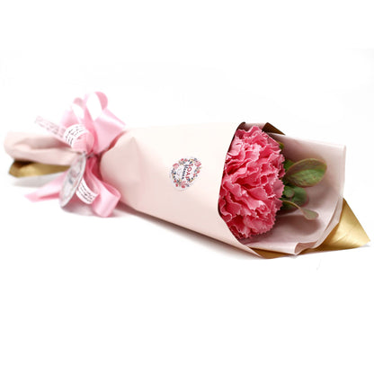 Bouquet of pink soap carnations wrapped in gold paper with a pink ribbon on a white background