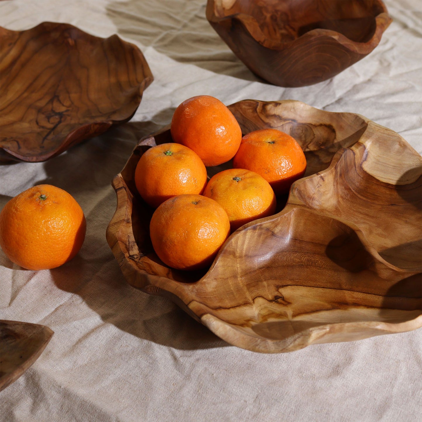 Smooth round teakwood fruit bowl with three divided sections, rich natural grain visible, filled with fresh fruit, nuts and snacks on a dining table in bright kitchen setting