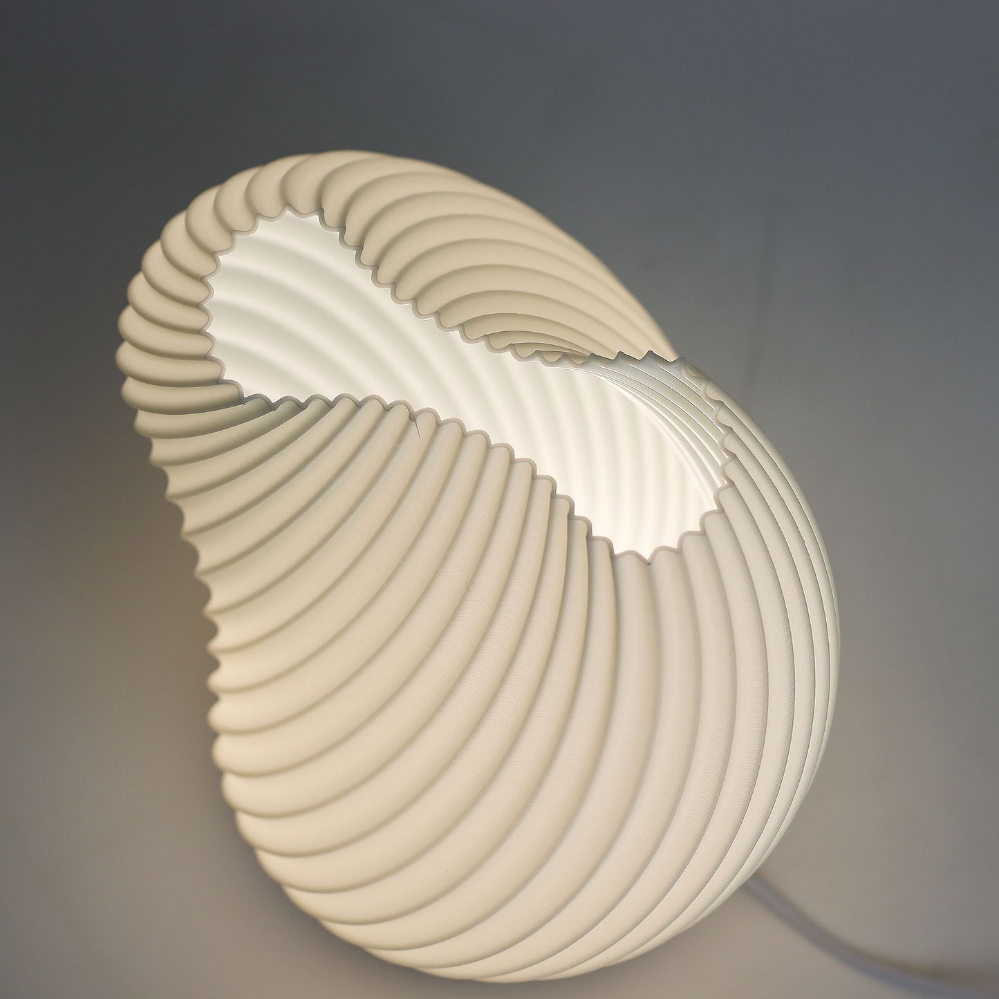Close-up of lamp’s textured honeycomb pattern and soft diffused light, showing elegant twisted shell-like silhouette and wooden base detail