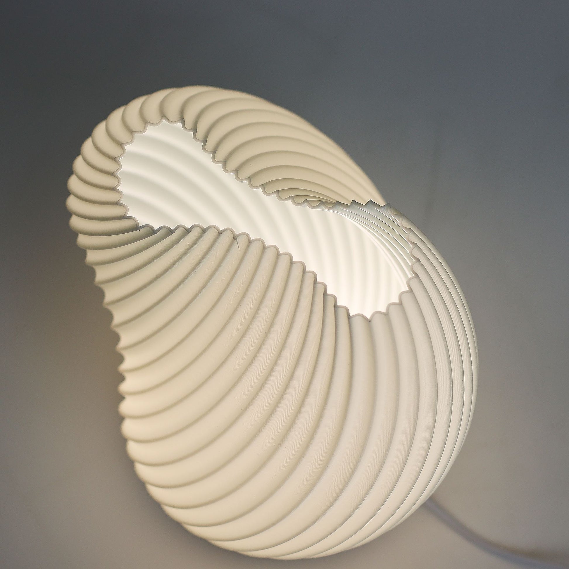 Close-up of lamp’s textured honeycomb pattern and soft diffused light, showing elegant twisted shell-like silhouette and wooden base detail