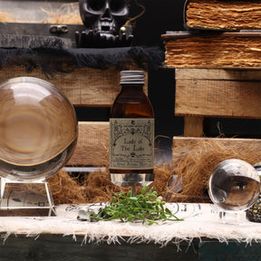 140ml amber glass bottle of Lady of the Lake ritual water with sword-in-lake label, surrounded by fresh basil, lemongrass, misty water and Excalibur sword
