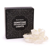 Clear quartz crystal fairy lights sparkling in glass bowl on meditation altar with sage, candles and moon phases in serene setting