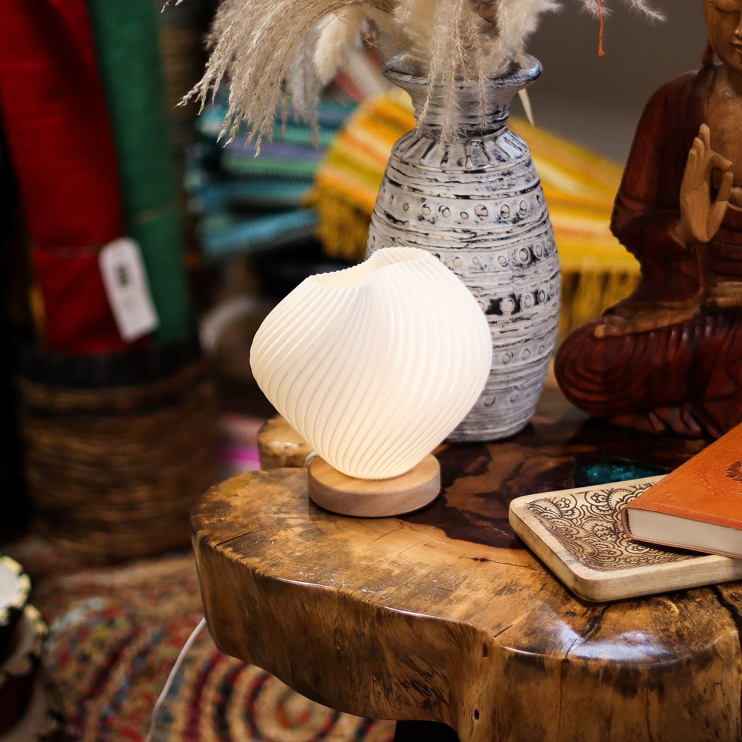 Decorative Shell Twisted New Wave USB lamp with textured honeycomb surface and elegant twisted shell-inspired shape, warm glow on 3rd brightness setting, placed on wooden base on a wooden surface with a vase and statue in the background