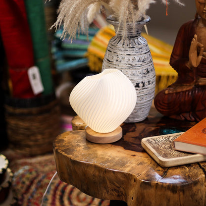 Decorative Shell Twisted New Wave USB lamp with textured honeycomb surface and elegant twisted shell-inspired shape, warm glow on 3rd brightness setting, placed on wooden base on a wooden surface with a vase and statue in the background