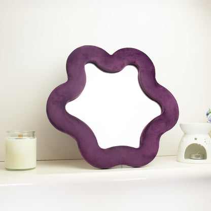 Soft squiggly star mirror in muted mauve velvet frame with gentle wavy edges, freestanding on white shelf with soft natural light reflecting in glass