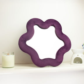 Soft squiggly star mirror in muted mauve velvet frame with gentle wavy edges, freestanding on white shelf with soft natural light reflecting in glass