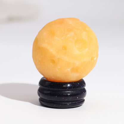40mm yellow jade Saturn sphere floating on shimmering goldstone ring stand, glowing against starry black background with subtle cosmic light