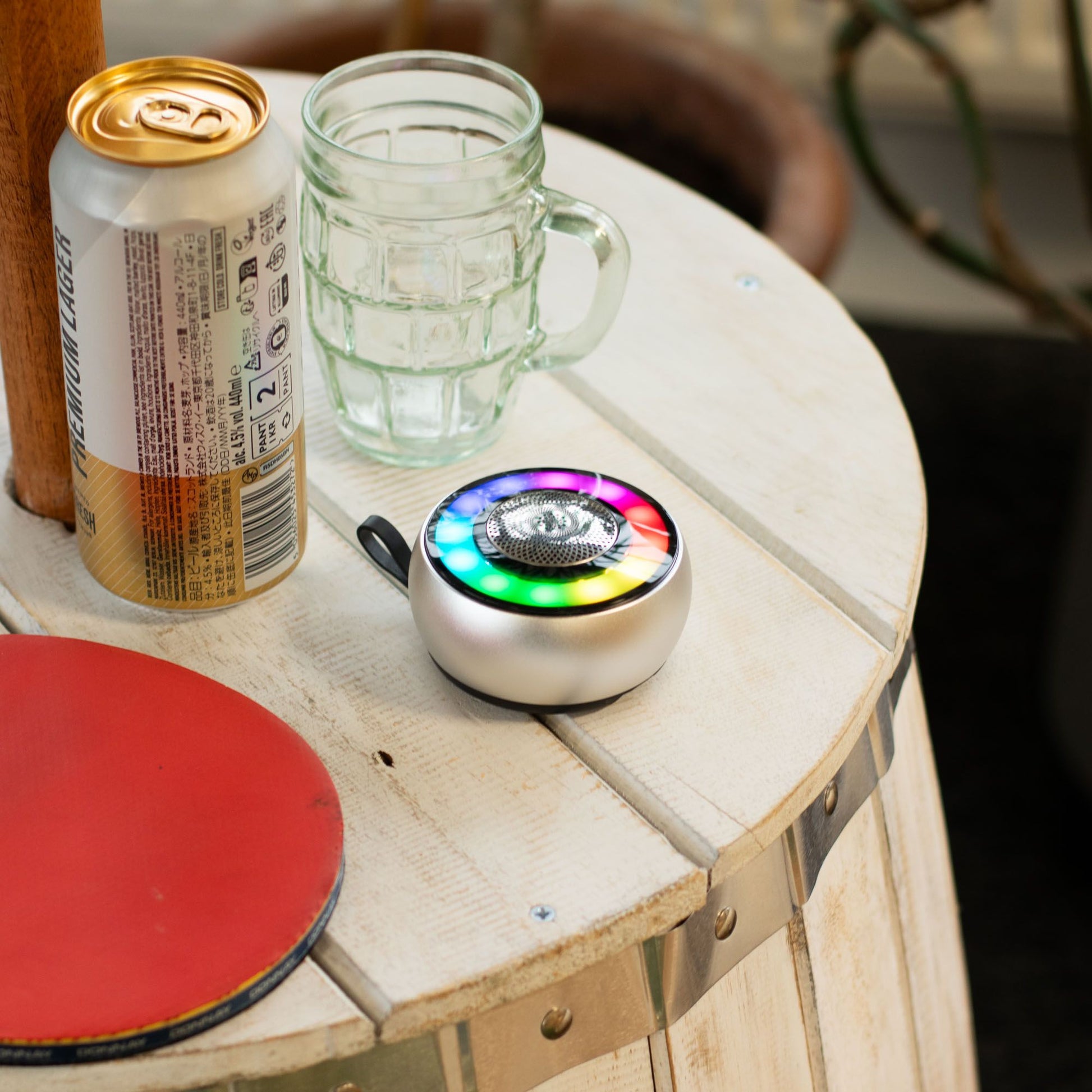 Silver Mandala mini speaker with glowing mandala LED light effect, compact circular design with carry loop, playing music on wooden desk with phone nearby