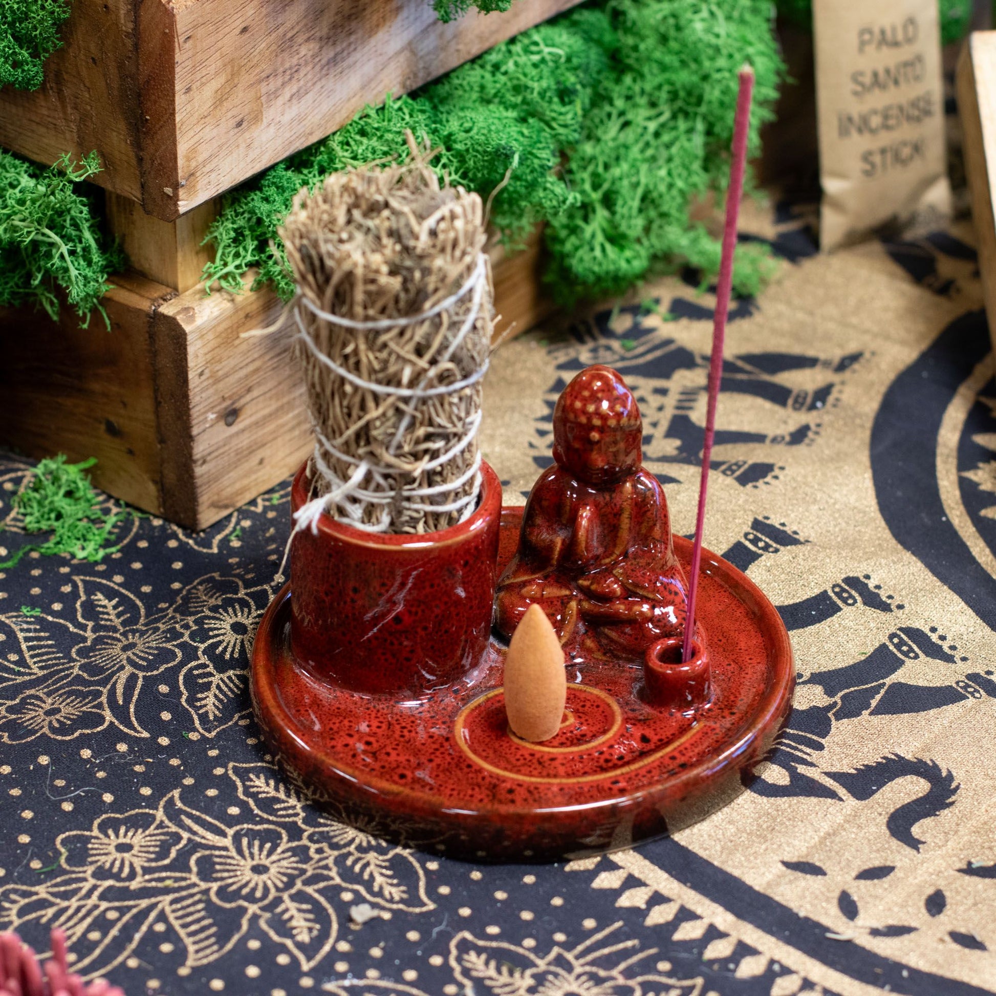 Red incense burner with Buddha statue and incense sticks on a patterned surface