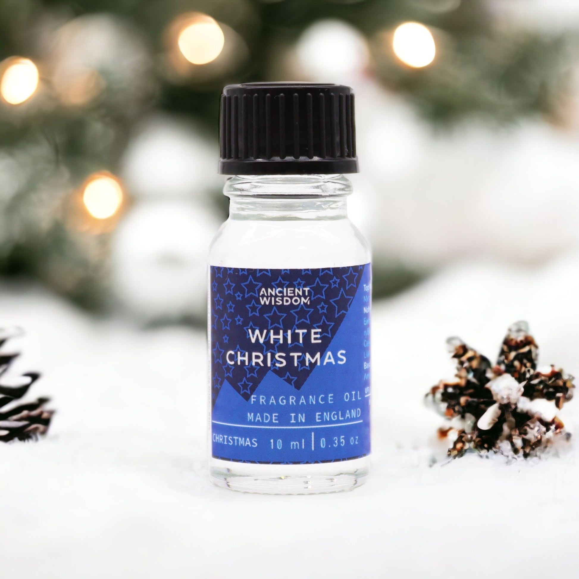 10ml White Christmas fragrance oil bottle surrounded by frosted pine, snowflakes and glittering snow on dark winter background