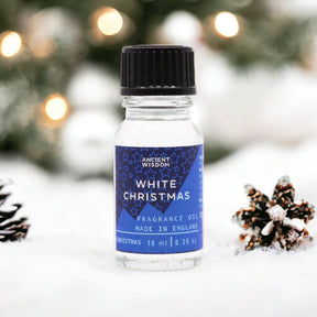 10ml White Christmas fragrance oil bottle surrounded by frosted pine, snowflakes and glittering snow on dark winter background