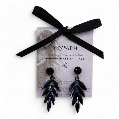 Jet black vintage glass long drop earrings catching firelight, styled against black velvet with glowing embers and obsidian stones