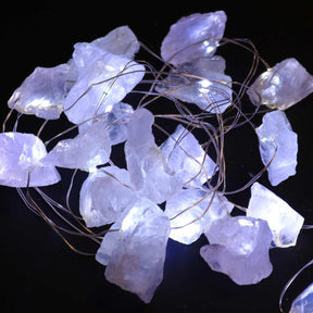 Clear quartz crystal fairy lights sparkling in glass bowl on meditation altar with sage, candles and moon phases in serene setting