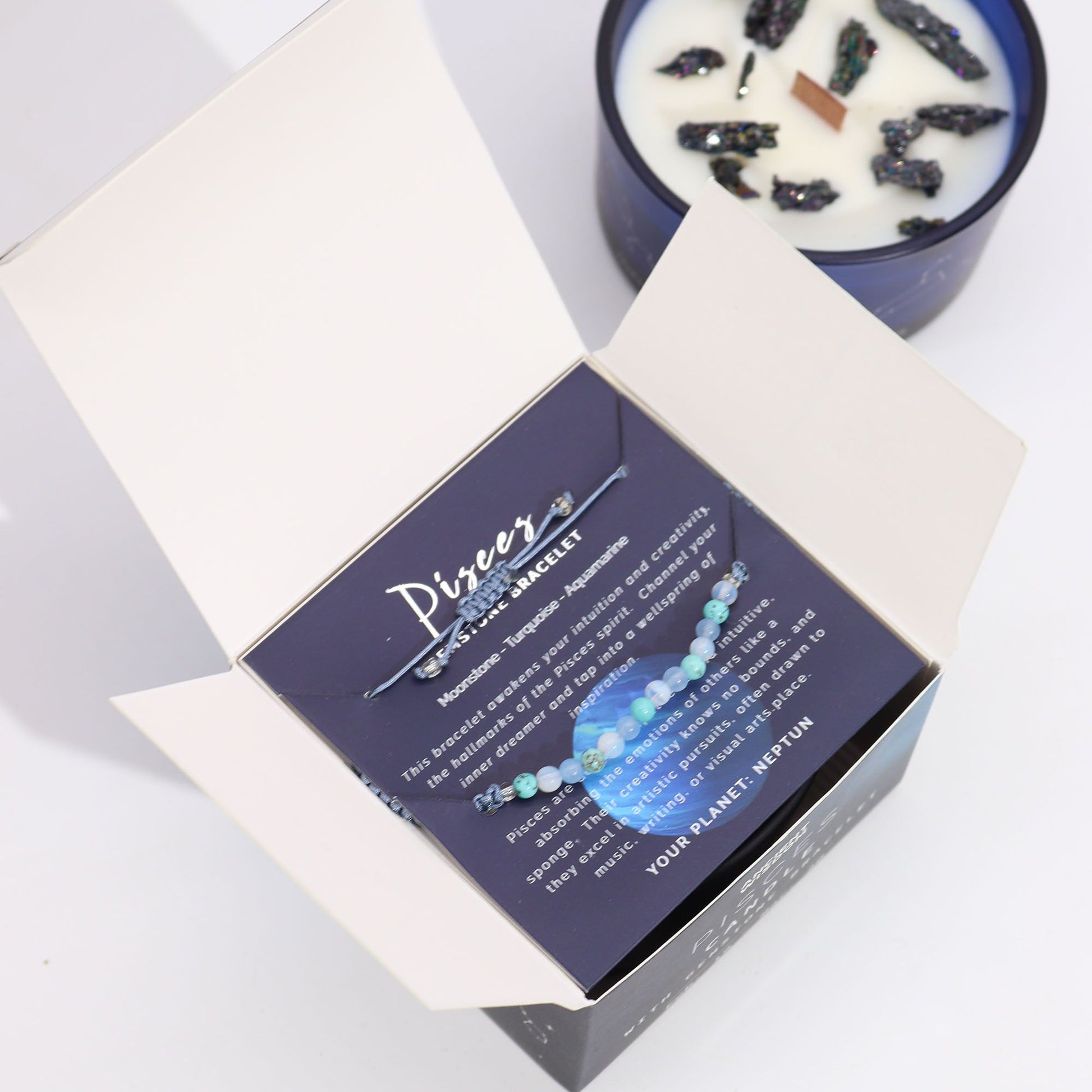 Soft aqua Pisces zodiac candle burning beside delicate moonstone, turquoise & aquamarine bracelet, styled with seashells