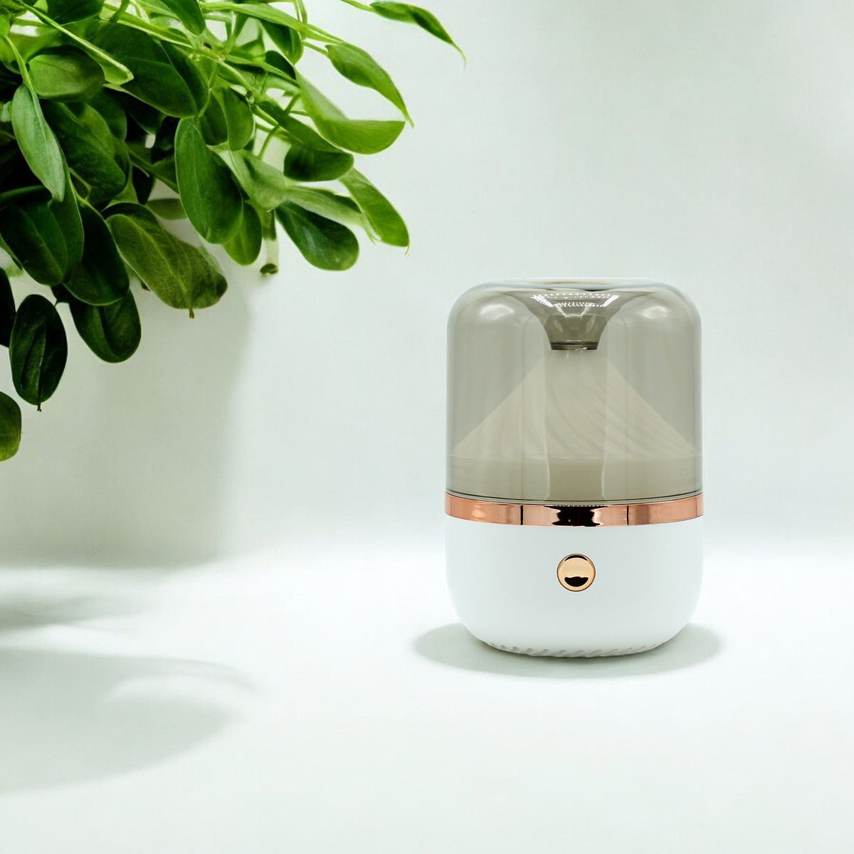 Small cylindrical humidifier with bronze accents on a white surface with a plant in the corner.