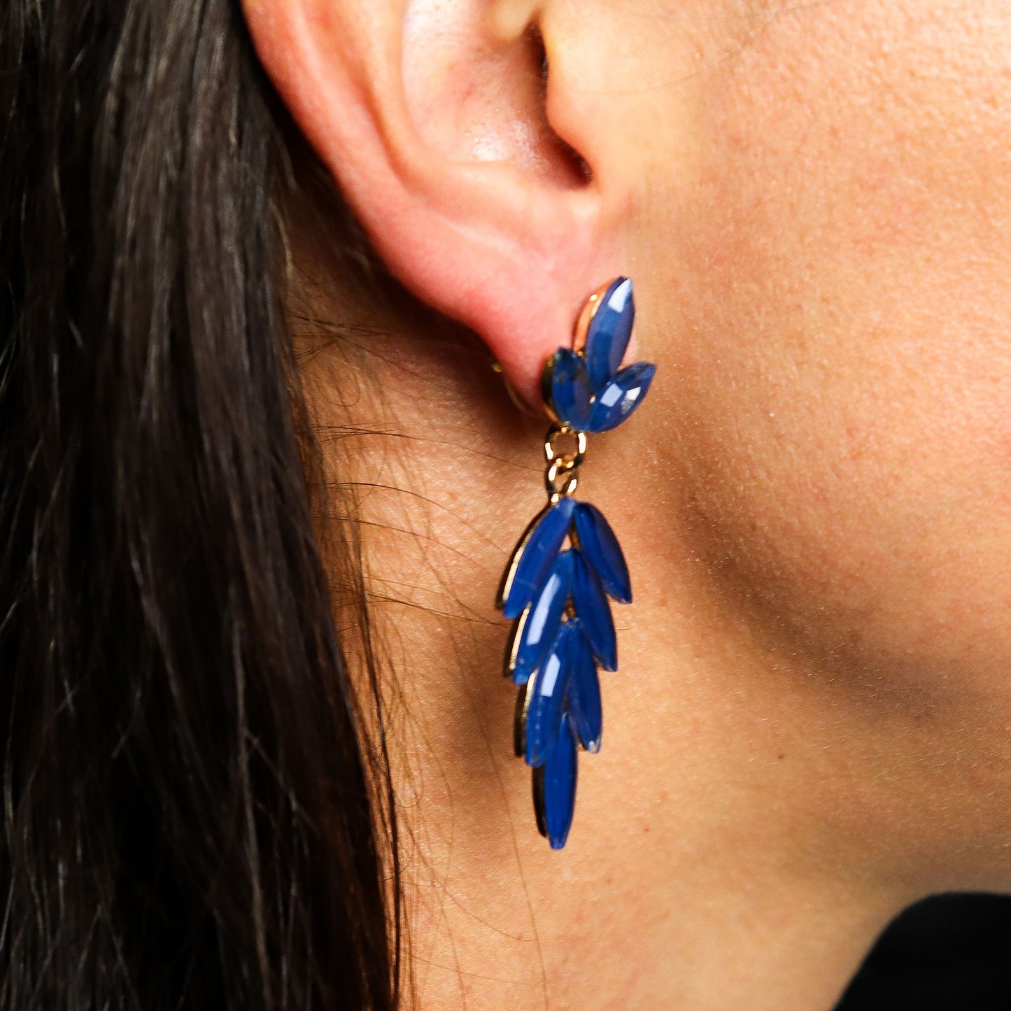 Close-up of a person wearing blue leaf-shaped earrings.