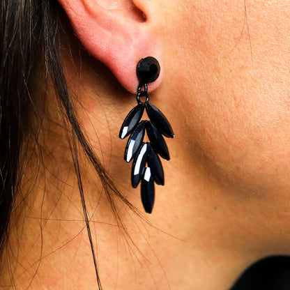 Jet black vintage glass long drop earrings catching firelight, styled against black velvet with glowing embers and obsidian stones