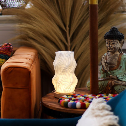 Decorative Star Twisted New Wave USB-C lamp with textured honeycomb surface and elegant star-inspired twisted shape, warm glow on 3rd brightness setting, placed on wooden base on a small table with a statue and colorful items in the background