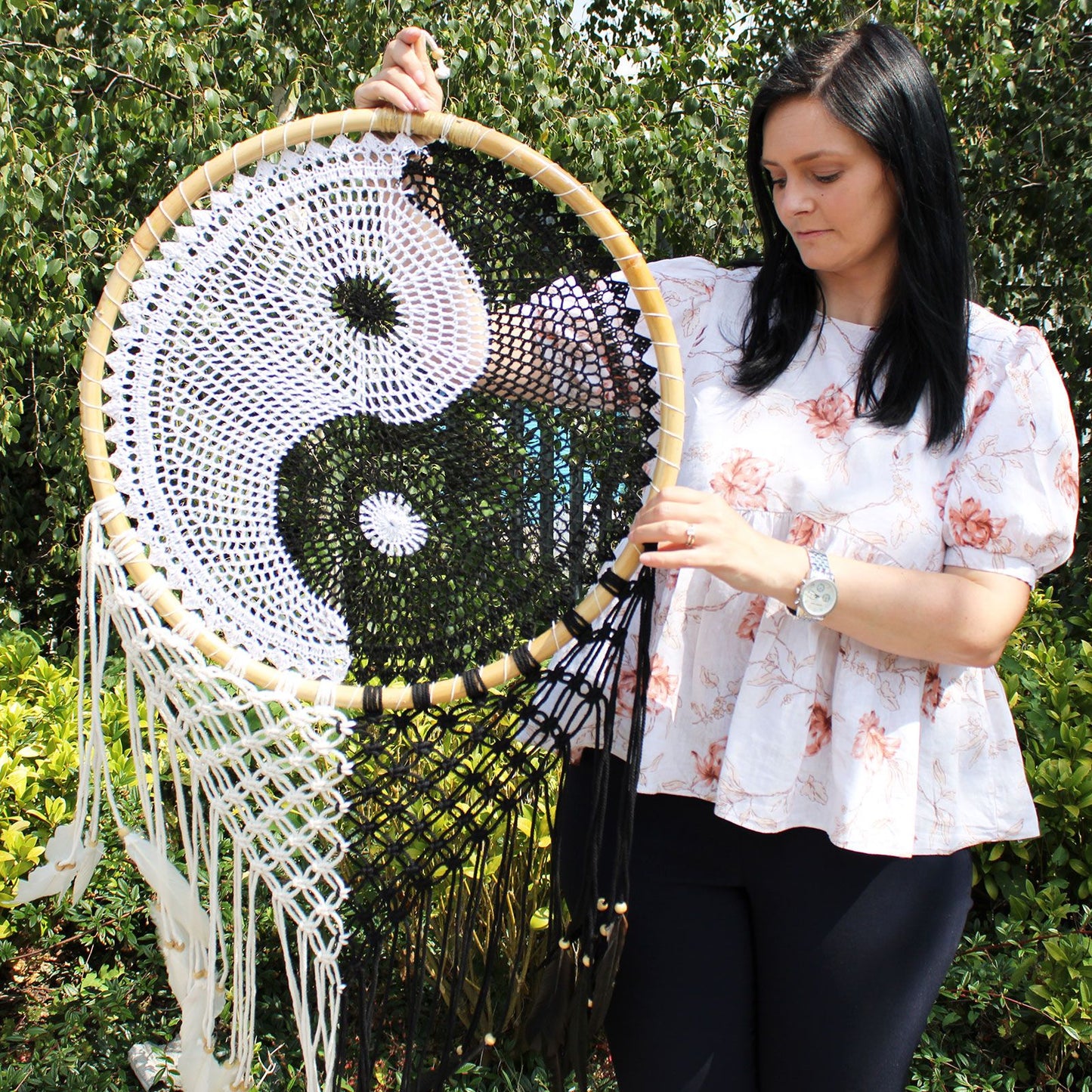 Extra large black and white Yin Yang dream catcher hanging above bed with flowing feathers and wooden beads against white wall