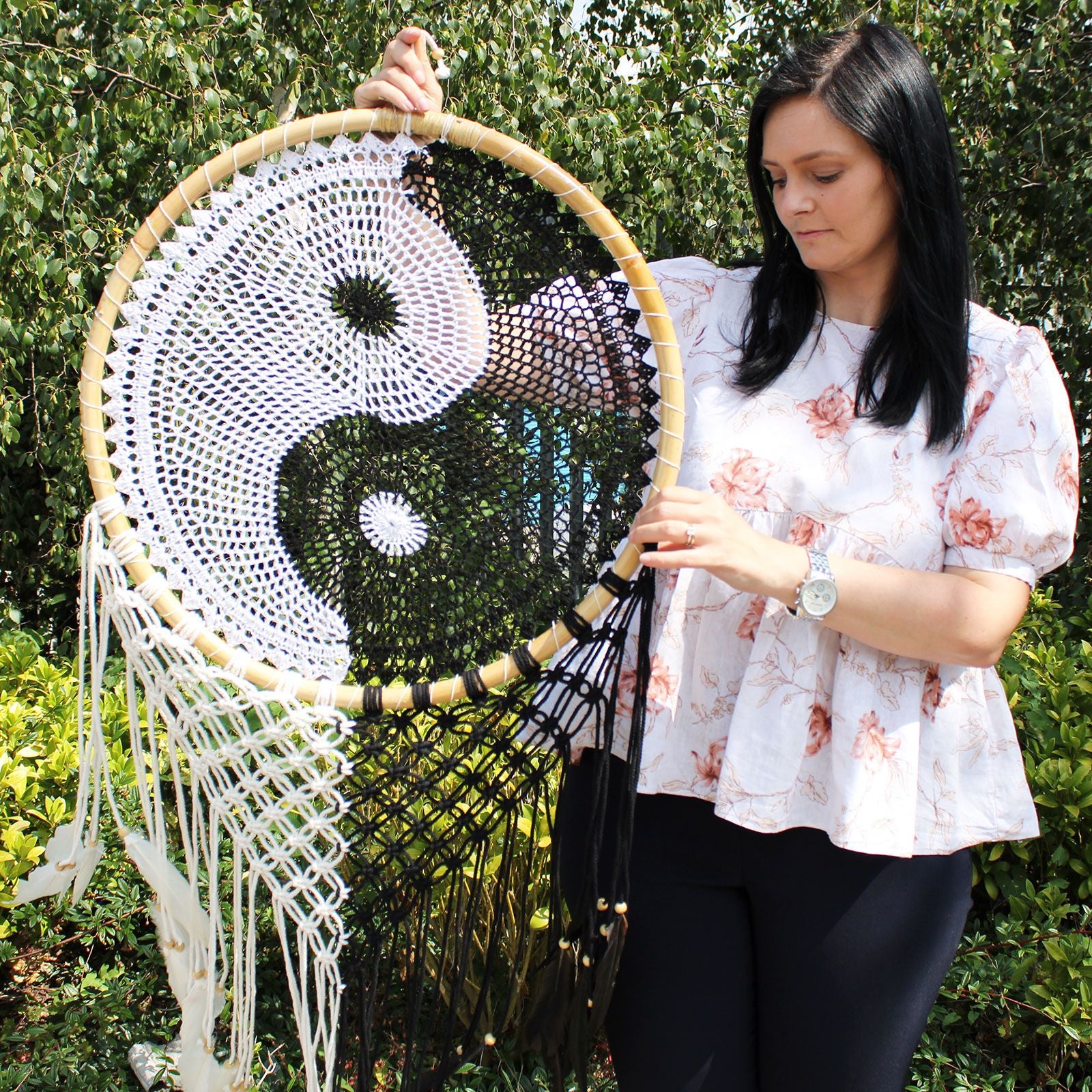Extra large black and white Yin Yang dream catcher hanging above bed with flowing feathers and wooden beads against white wall