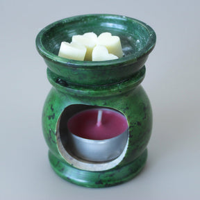 Green ceramic oil burner with wax cubes and a candle on a beige background