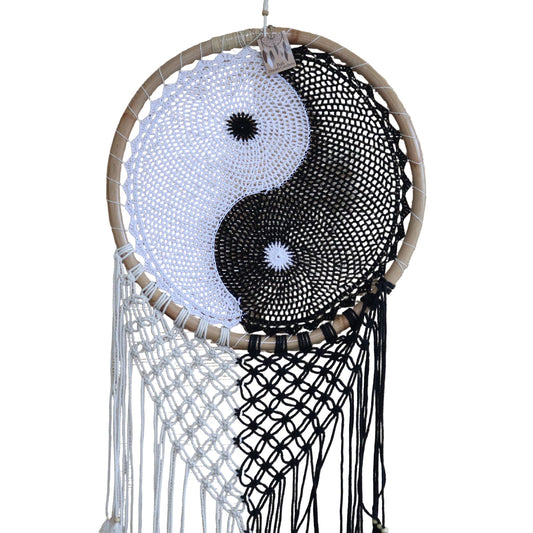 Extra large black and white Yin Yang dream catcher hanging above bed with flowing feathers and wooden beads against white wall