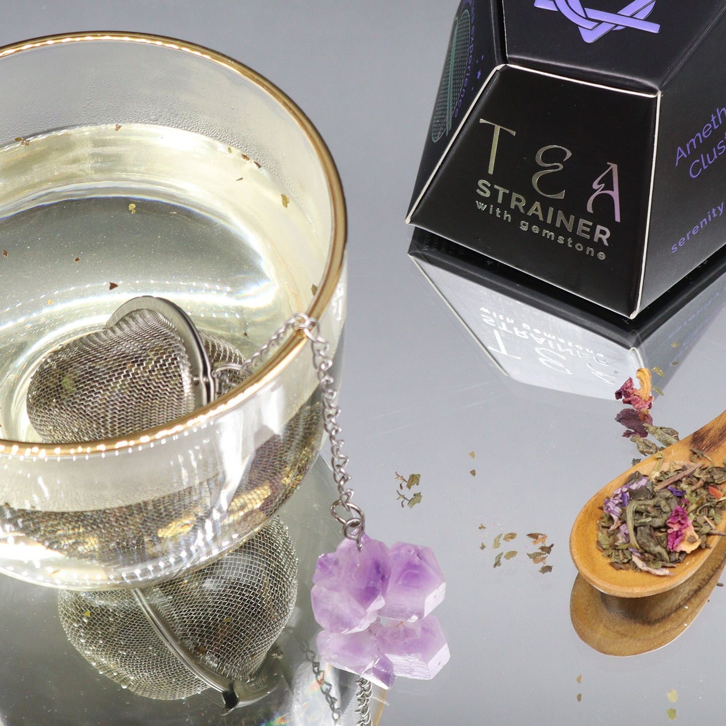 Tea strainer with gemstones next to a box labeled 'Tea Strainer with gemstones' on a reflective surface.